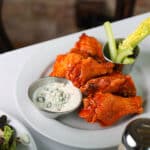 Spicy Buffalo wings served on a white plate with blue cheese dipping sauce.