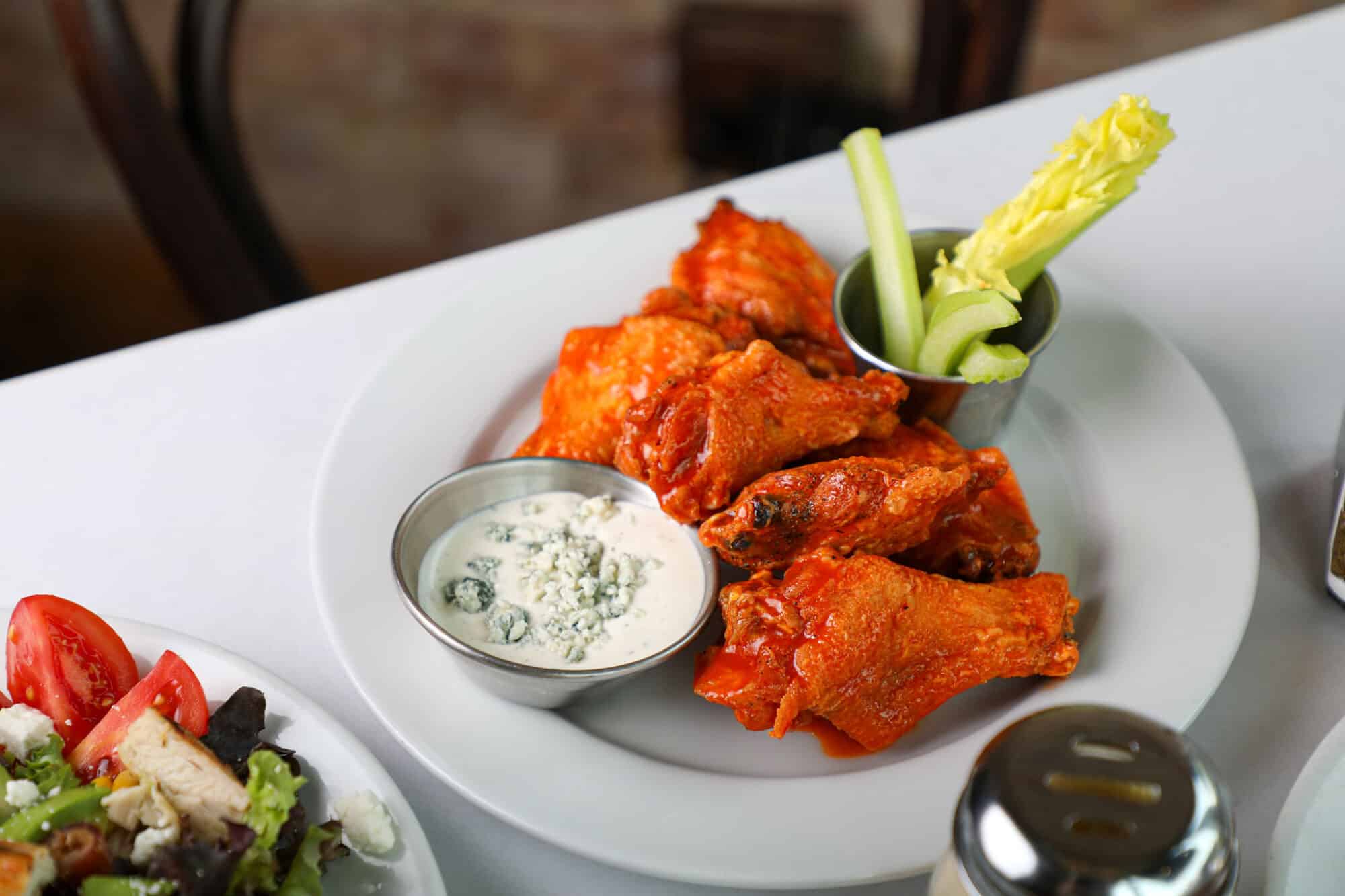 Spicy Buffalo wings served on a white plate with blue cheese dipping sauce.